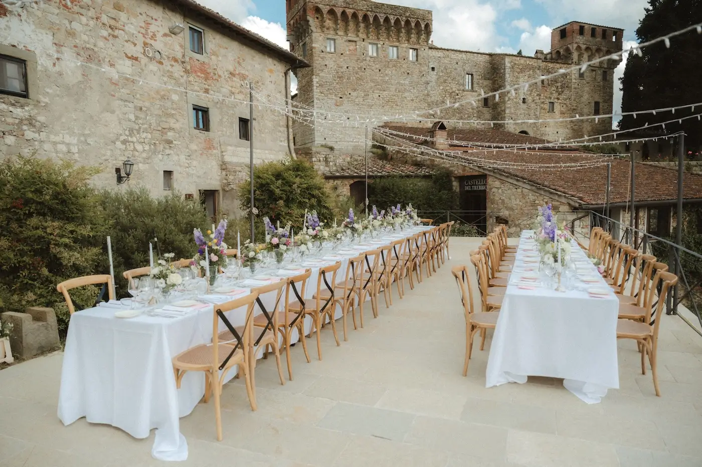 Long outdoor reception tables set in a historic Italian courtyard surrounded by stone buildings.