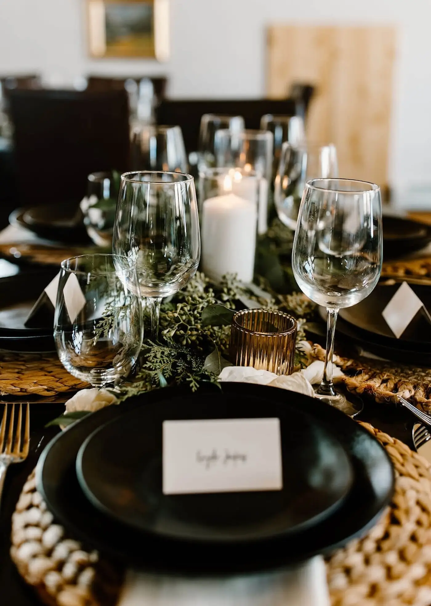 Elegant winter wedding table setting with black plates, greenery, and candlelight centerpiece.