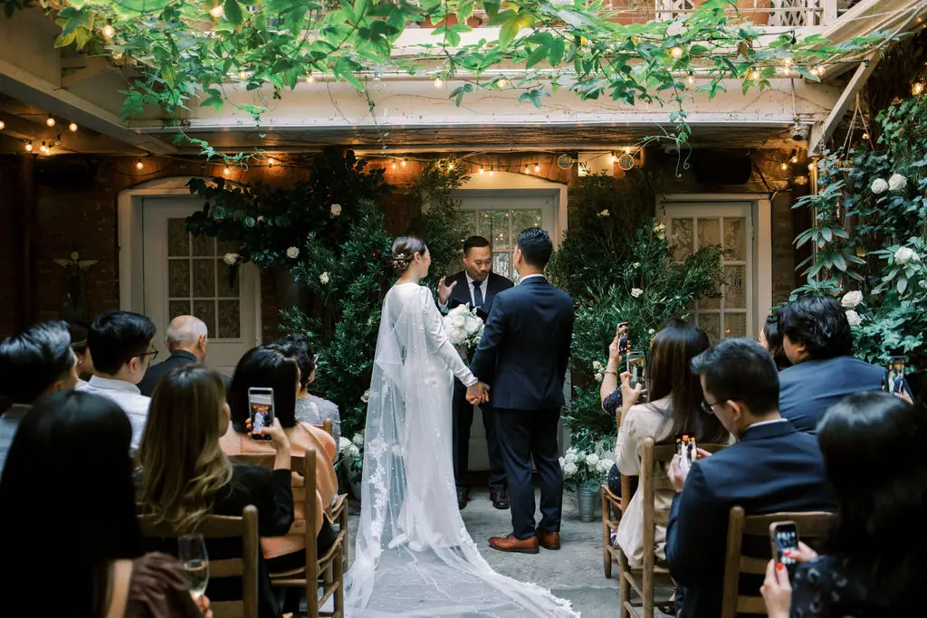 Couple exchanging vows during an intimate courtyard micro wedding ceremony surrounded by greenery and seated guests.