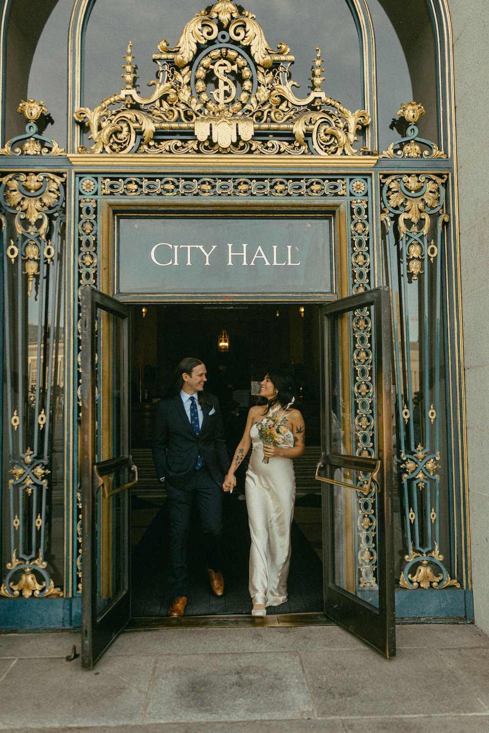 Couple exiting City Hall after an intimate micro wedding ceremony with ornate architectural details and open doors.