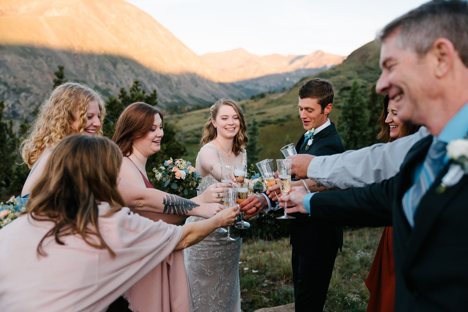Mountain micro wedding champagne toast at sunset, couple and a small group clinking flutes with golden-lit Rocky Mountain peaks behind them