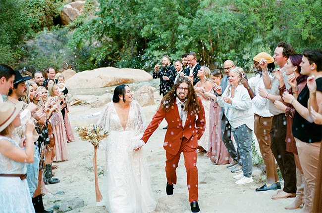 Bohemian outdoor recessional through a confetti toss, bride in white lace with dried bouquet, groom in rust suit, guests in earth tones cheering