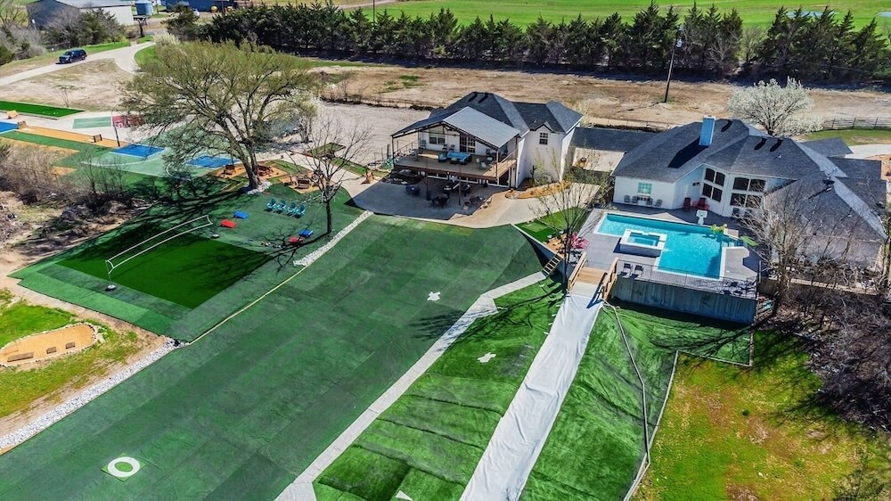 Aerial of a North Texas VRBO wedding estate with two homes, expansive lawn featuring a long slip-and-slide, sport courts, and a putting green