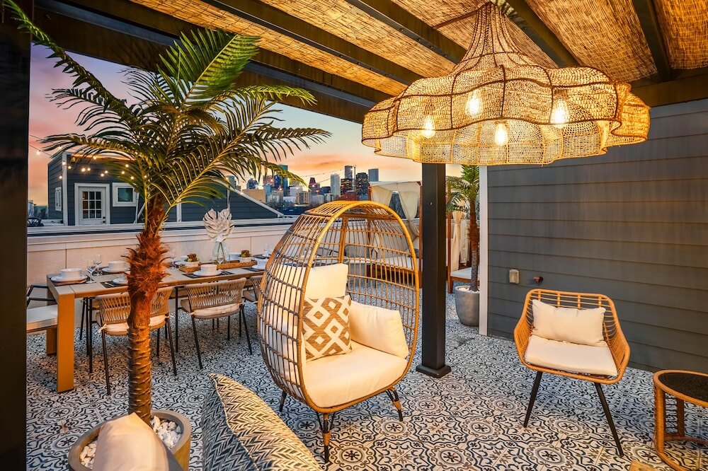 Rooftop terrace at a Houston VRBO wedding venue with patterned Mediterranean tile, a rattan egg chair and pendant chandelier, skyline at sunset