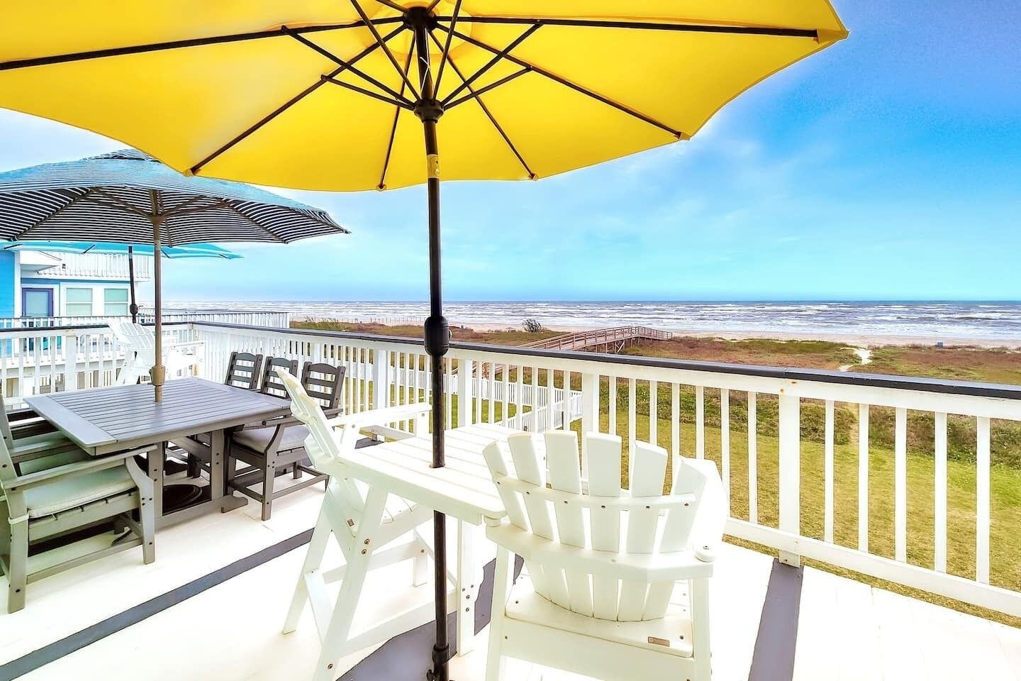 Beachfront deck at a Galveston VRBO wedding venue with yellow patio umbrella, Adirondack chair, and table overlooking dune grass and the Gulf