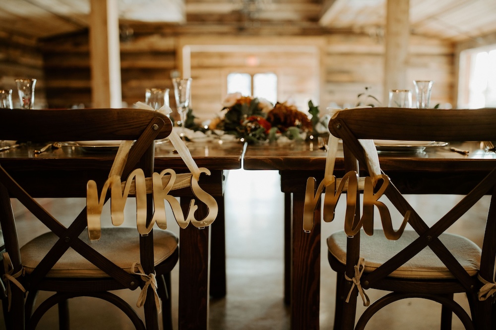 Sweetheart table at a Texas VRBO wedding venue, two dark crossback chairs with 'mr' and 'mrs' signs, dusty florals running down the linen runner