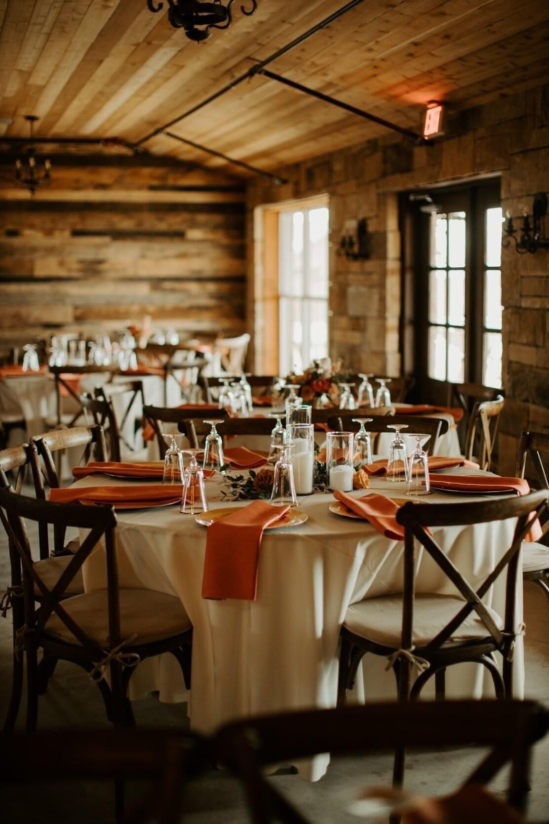 Indoor barn reception at a Dallas VRBO wedding venue, round tables with terracotta napkins, candles and florals, dark crossback chairs, wood walls