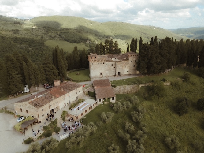 Aerial of a Tuscan castle micro wedding venue with crenellated stone tower, cypresses lining the property, lower farmhouses, rolling Chianti hills