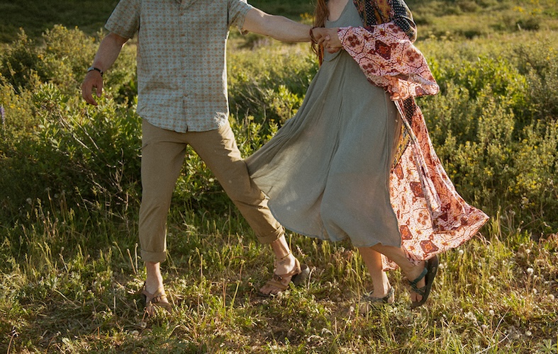 Couple walks through tall yellow wildflowers with sweeping Crested Butte alpine landscape behind them