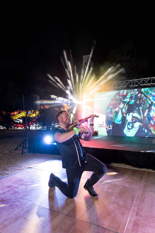 Electric violinist Jared Judge mid-performance with a custom electric violin and concert lighting behind him