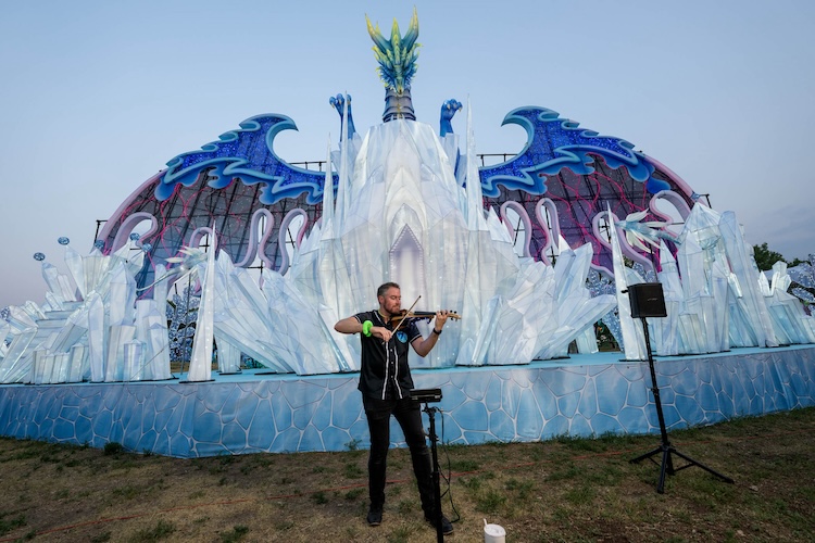 Jared Judge playing electric violin at a wedding ceremony with a string-lit outdoor reception space behind him
