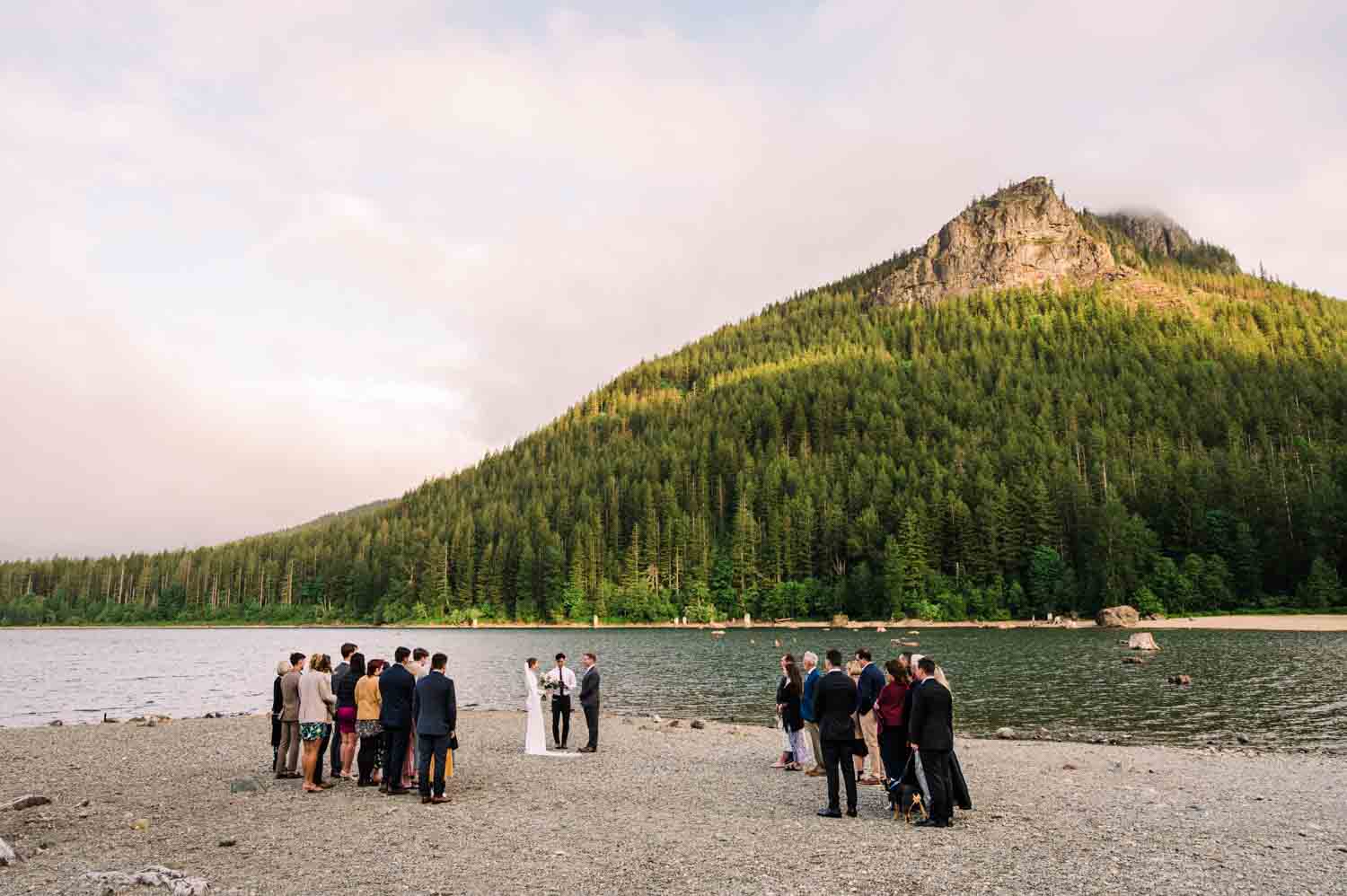 Couple stands at a lakeside micro wedding ceremony with calm water and a wooded shoreline behind them