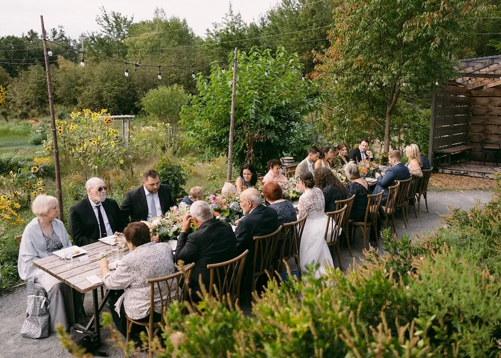 Guests gathered around long wooden tables for an intimate outdoor brunch wedding reception at a garden café with string lights and lush greenery.