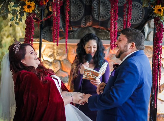 Couple shares a laugh during their winter wedding ceremony, surrounded by autumn-toned foliage
