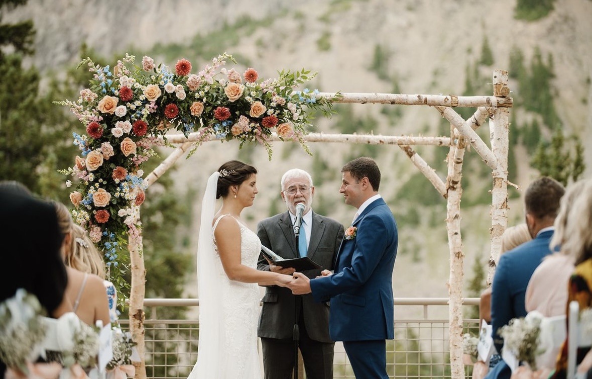 A couple says their vows in front of a wedding arch at their small wedding