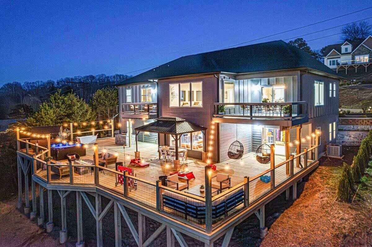 Modern multi-level Asheville home at twilight, elevated deck with hot tub, gazebo dining, hanging egg chairs and string lights overhead
