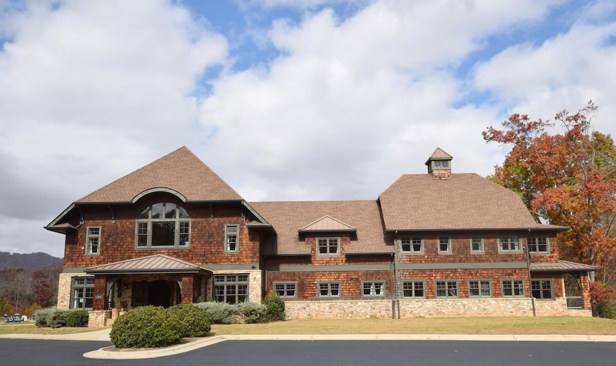 Cedar-shake VRBO wedding lodge with stone foundation, arched Palladian window over a stone-columned entry porch, copper cupola, autumn maple at right