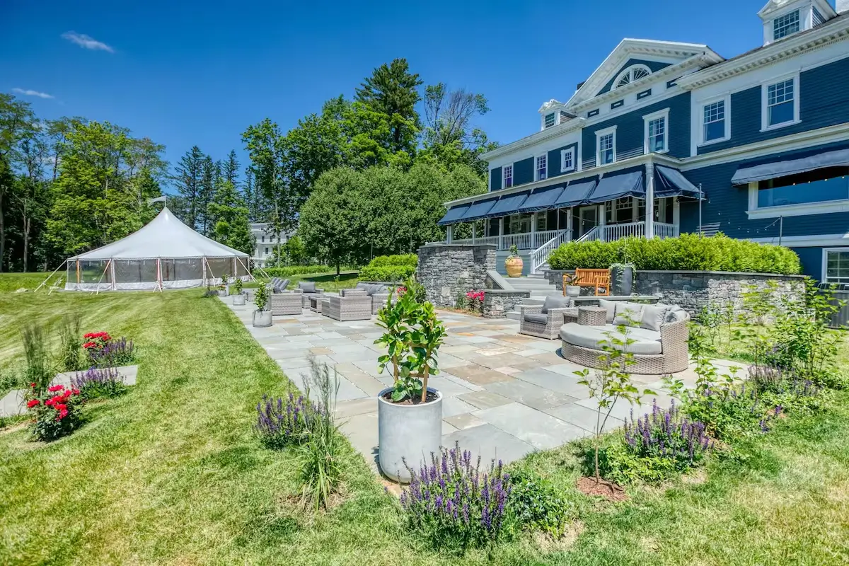 Navy Gilded Age VRBO wedding venue in the Berkshires, white pediment and awnings, flagstone patio of wicker lounges, white sailcloth tent on the lawn