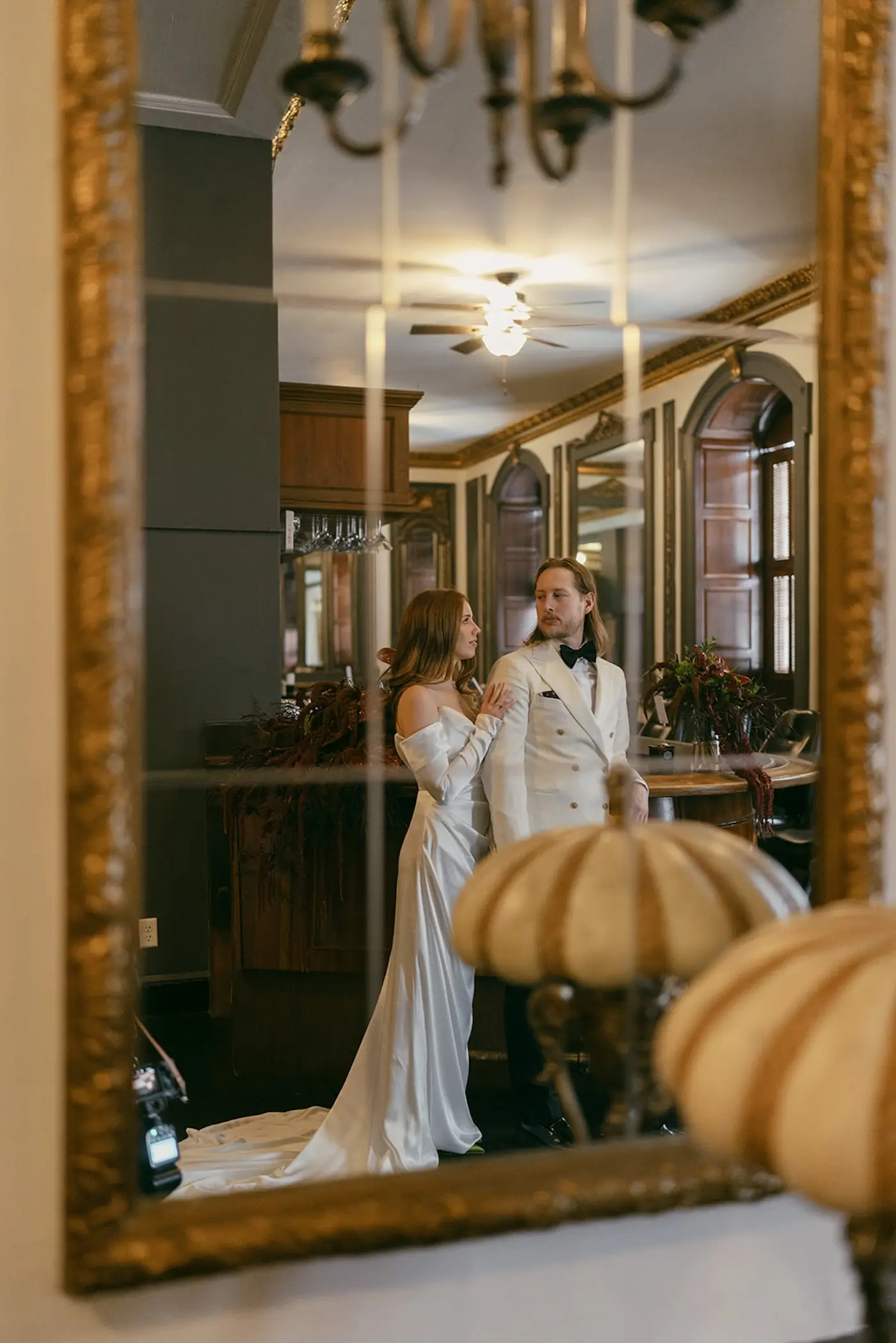 Bride and groom standing together in bar reflected in ornate mirror during elegant wedding photos.