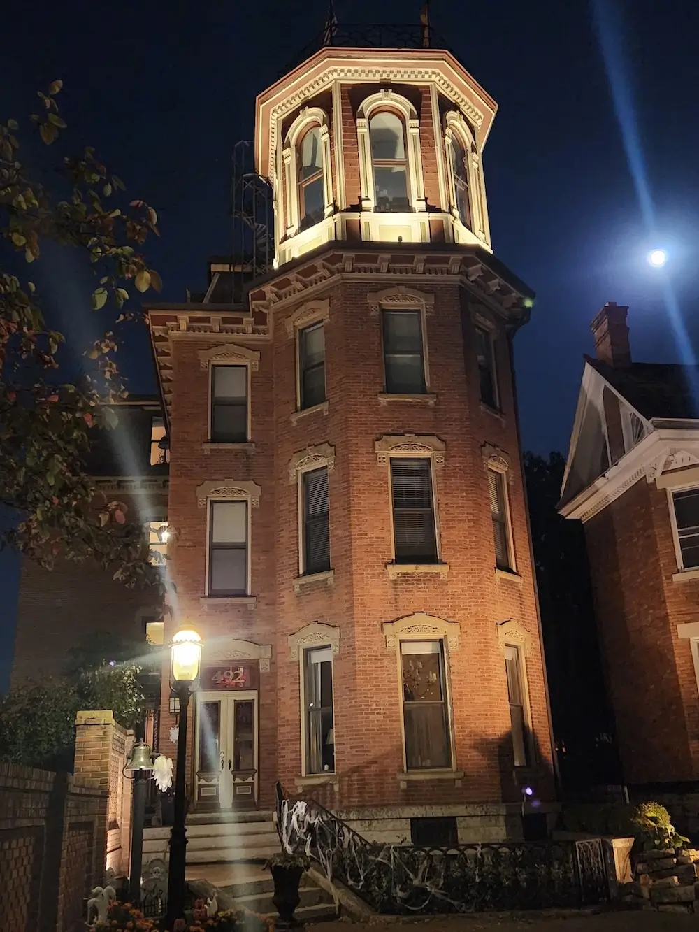 Italianate brick castle Columbus VRBO wedding venue at night, four-story octagonal tower, near-full moon, gas lamp at the front steps, German Village