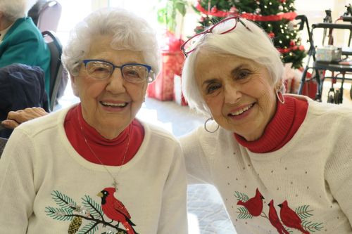 Two elderly women enjoying each other's company in holiday sweaters.