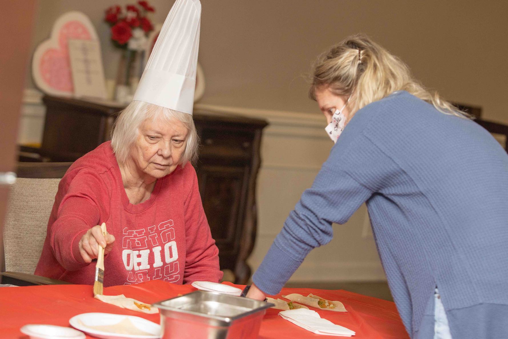 An elderly woman in a red Ohio t-shirt using a basting brush to put sauce on a lobster.