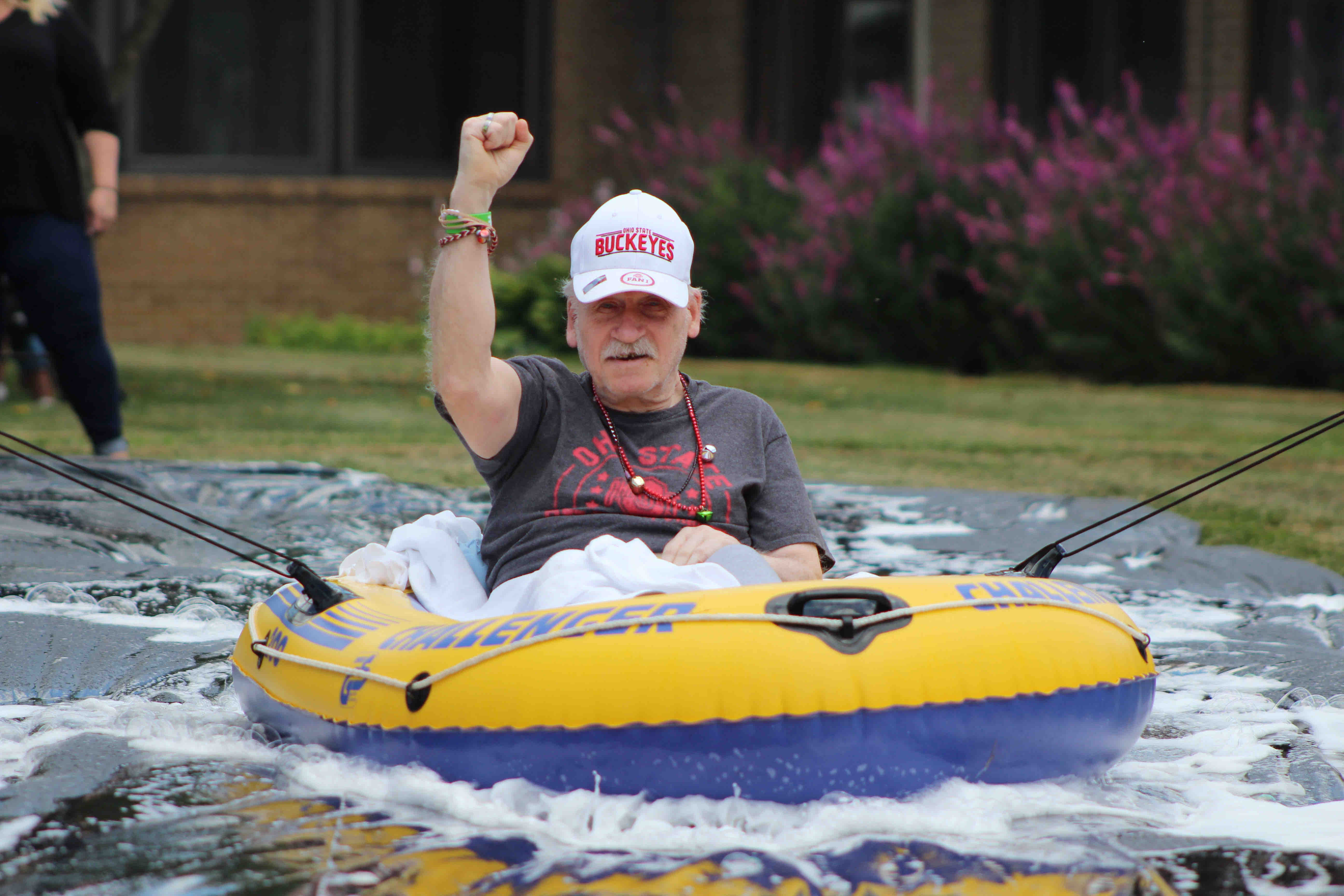 Elderly man in OSU apparel on a slip-n-slide inner-tube with a fist raised for this awesome senior activity.