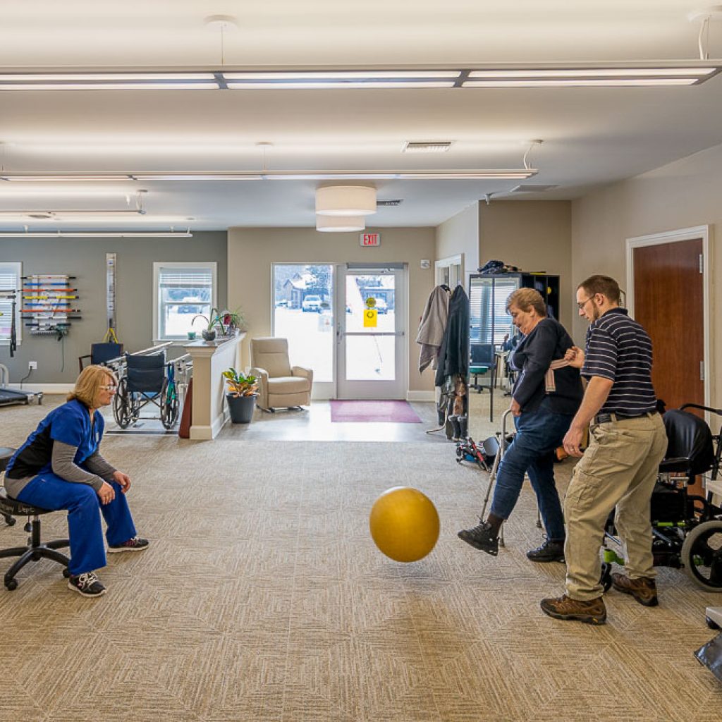 A physical therapists works on an exercise kicking an exercise ball with two patients.