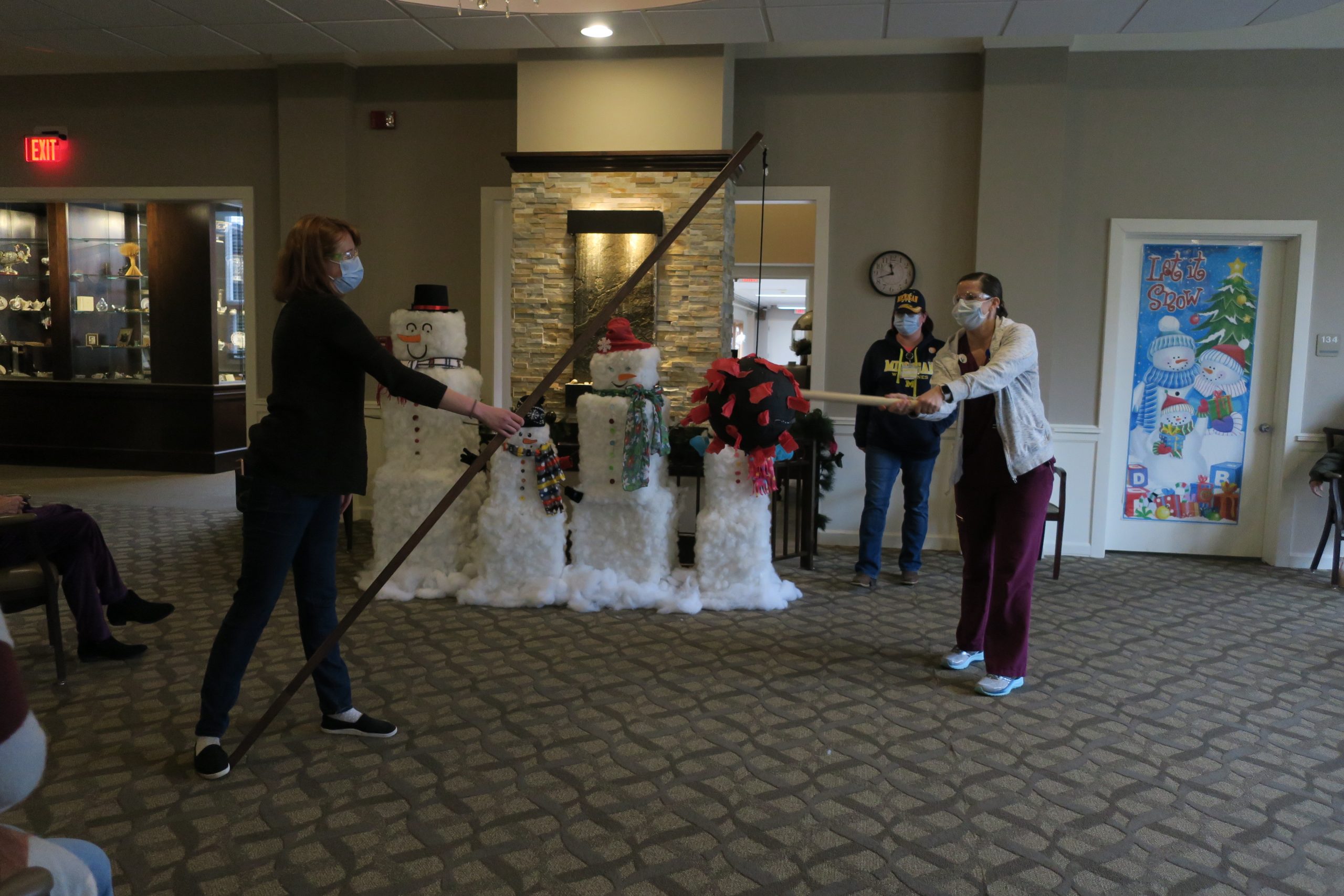 One person holds a COVID-themed pinata while another swings at it.