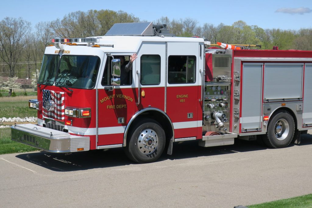 A fireman waving from firetruck driver's seat.