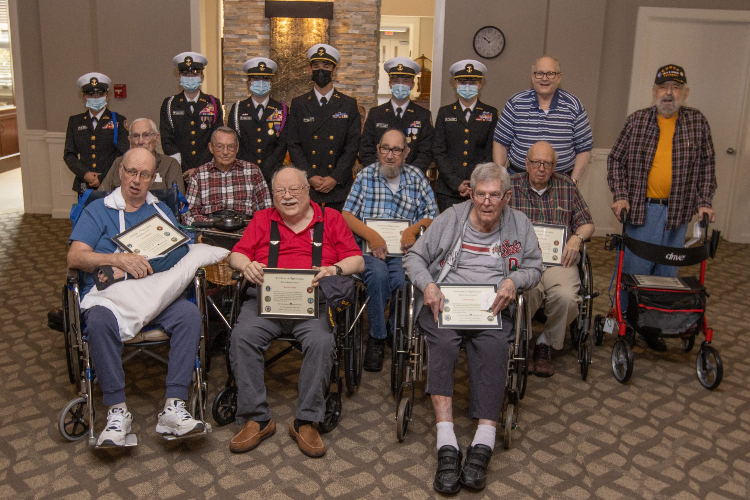 Nine senior veterans stand and sit in front of six Navy Junior ROTC members on Veterans Day 2021.