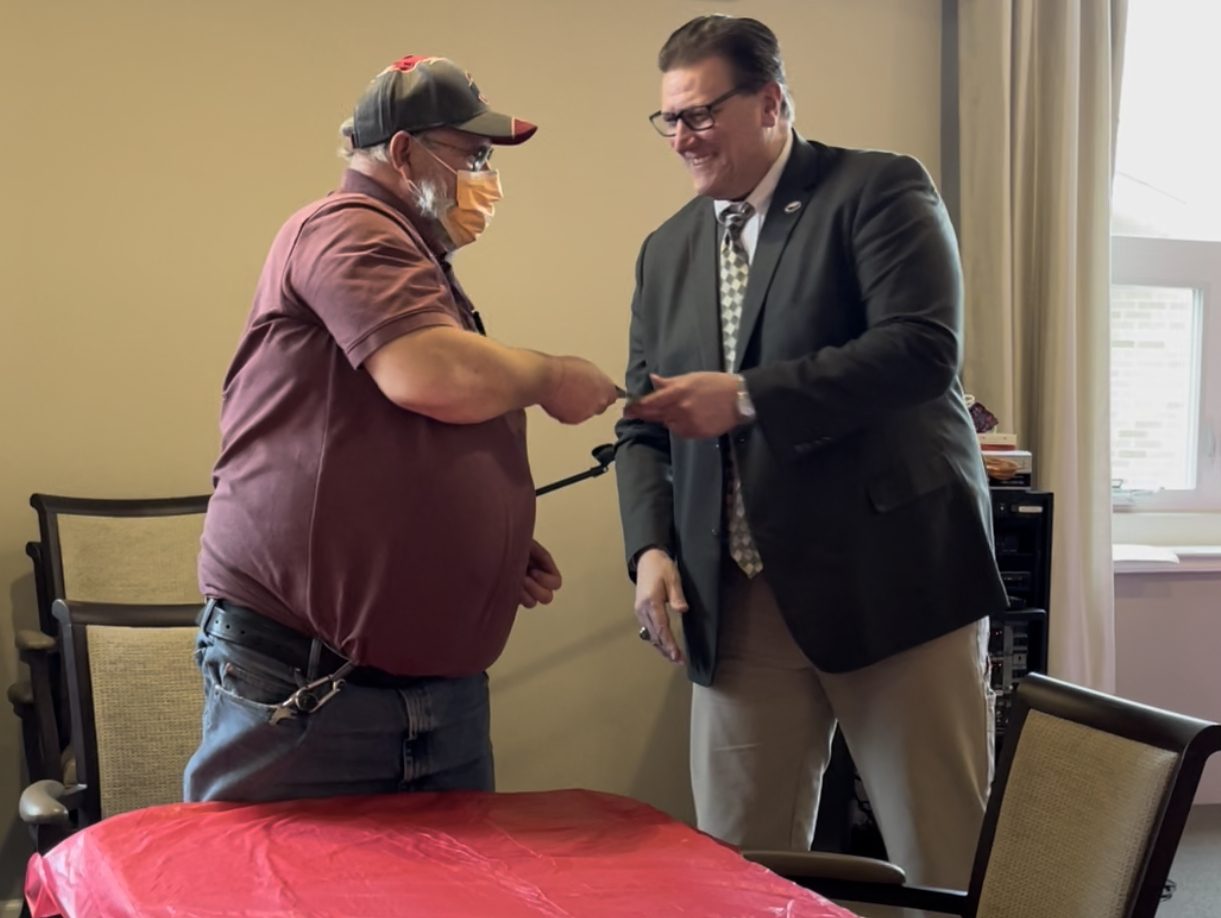 Mayor Matt Star shakes the hand of a man in a red shirt, face mask, and ball cap.