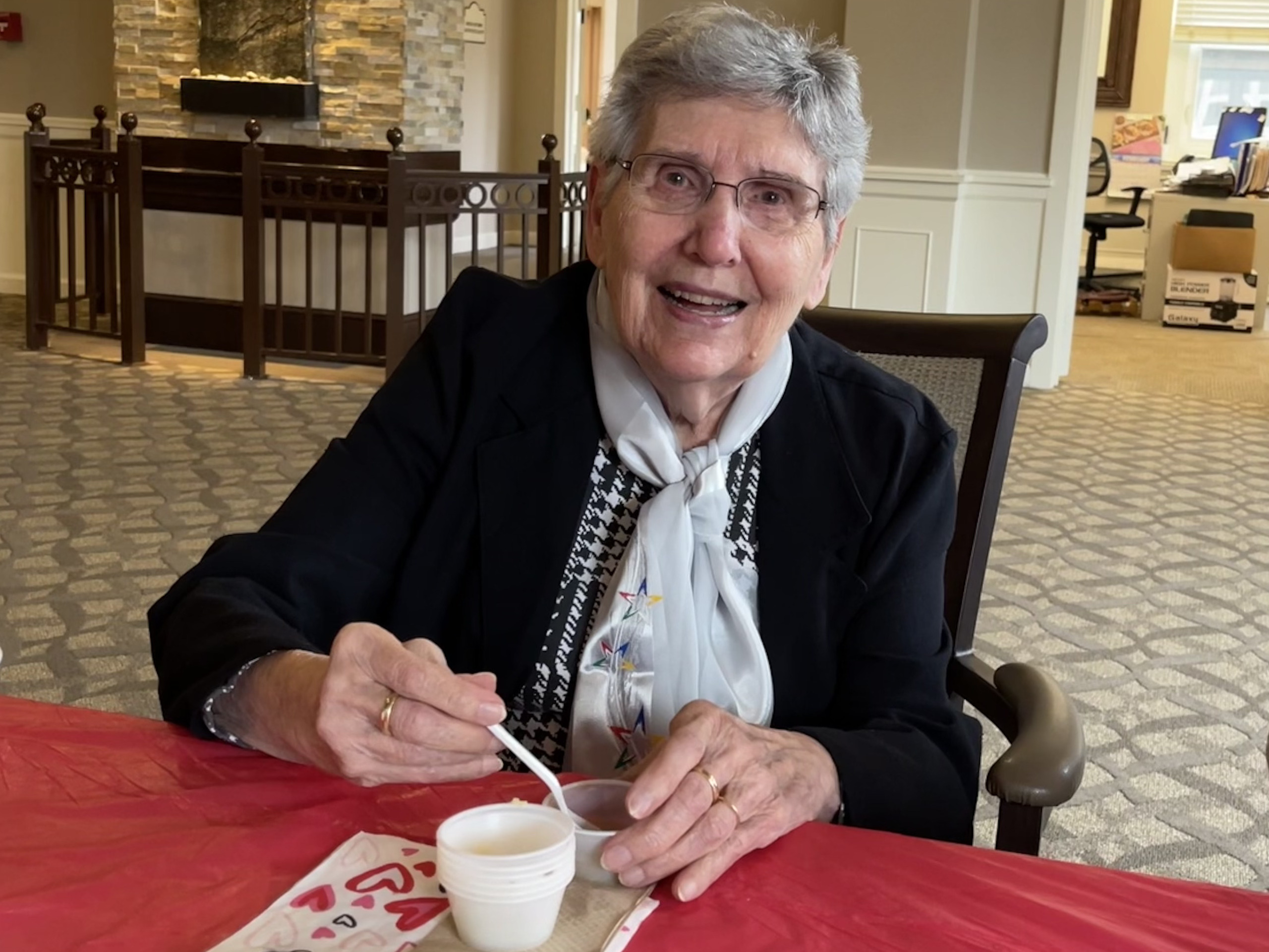A smiling woman eating soup.