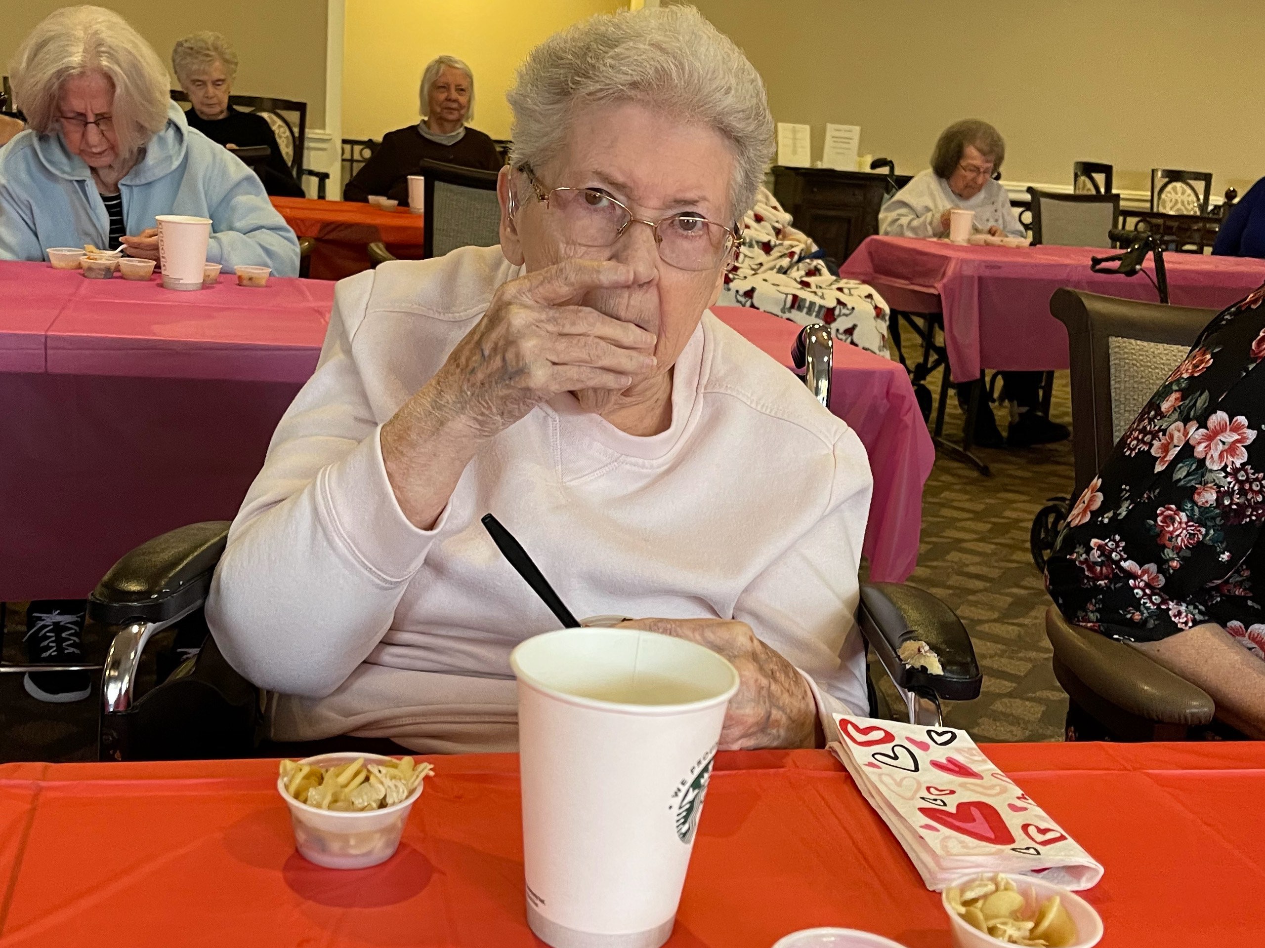 A senior woman holds a cup of soup up to her lips.