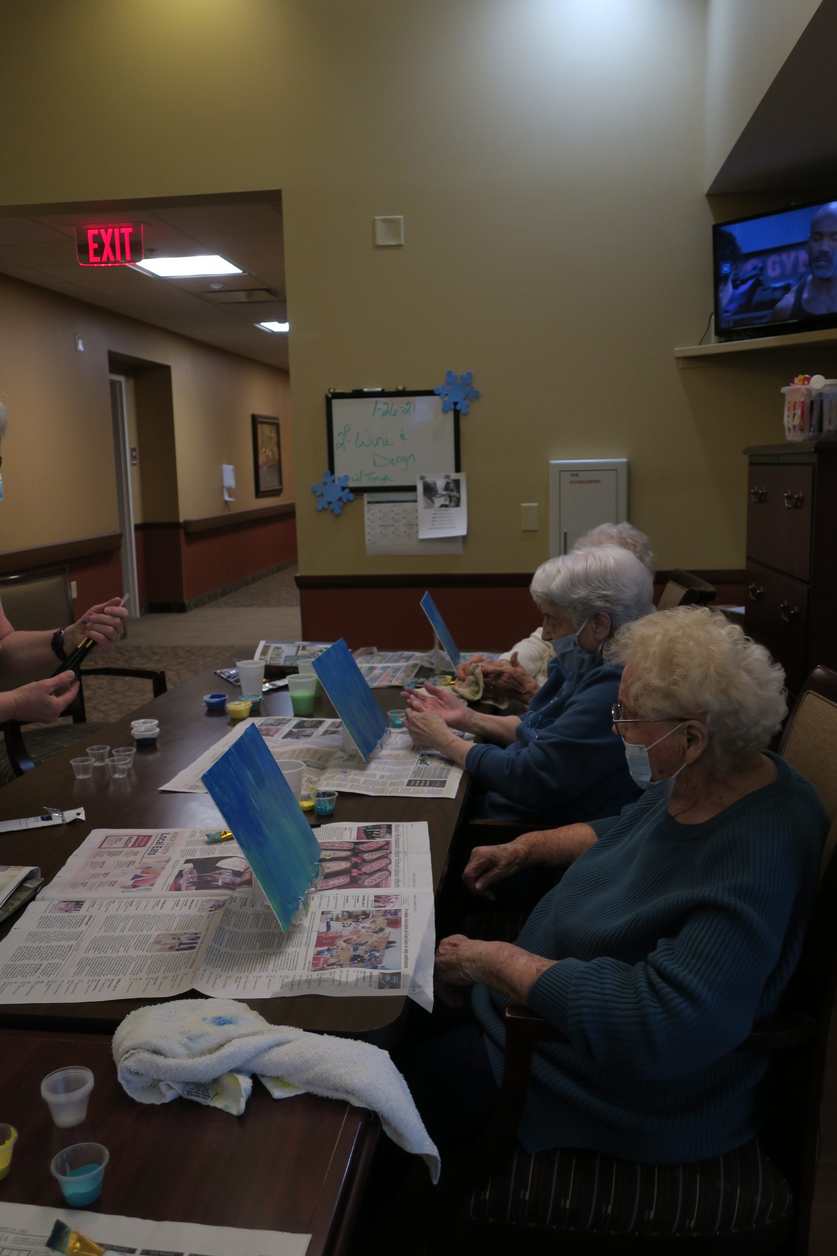 Three senior women sitting at a table and painting blue watercolors on canvases.