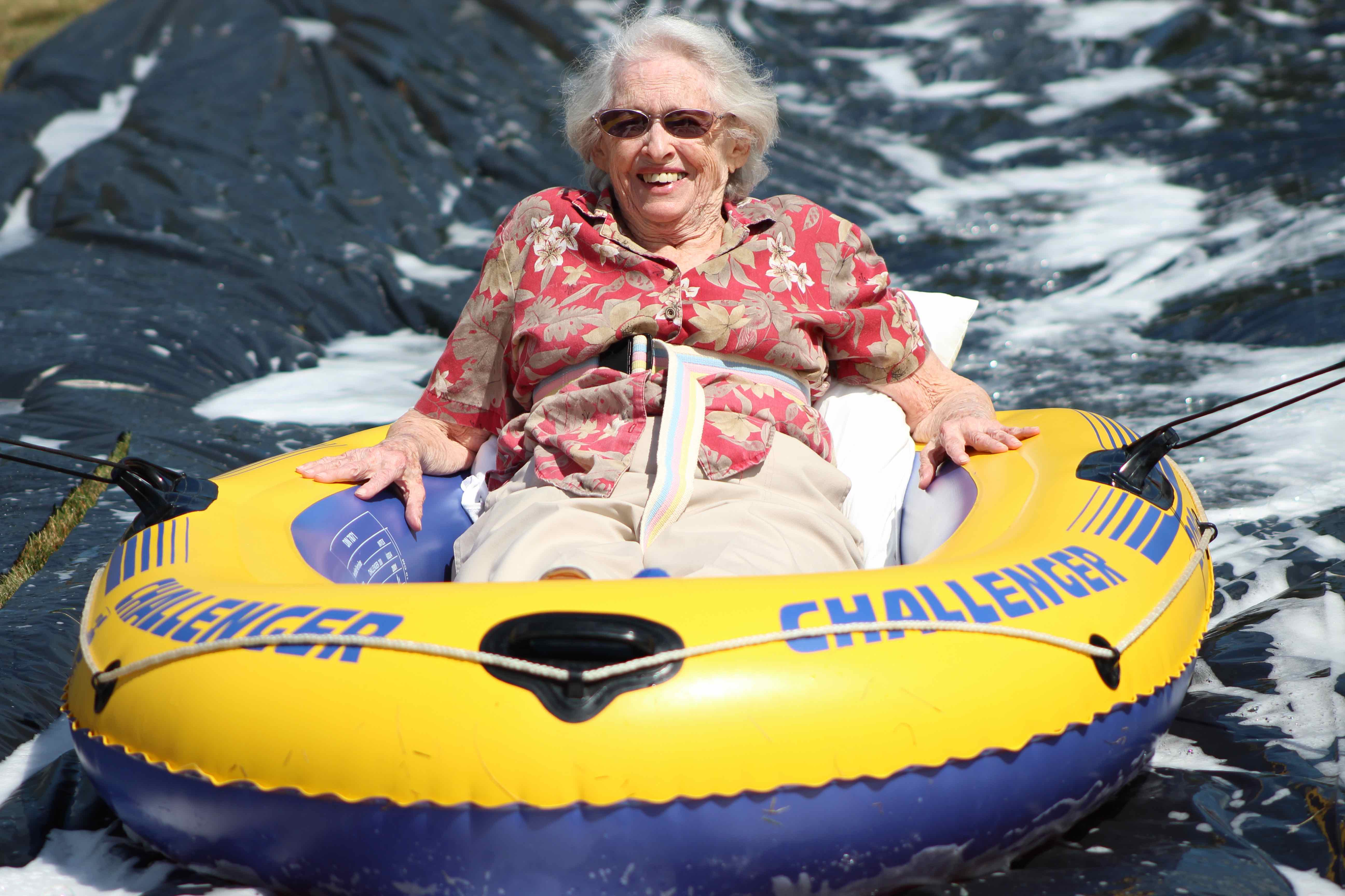 Elderly woman in floral shirt smiling ear to ear on an inner-tube slip-n-slide.