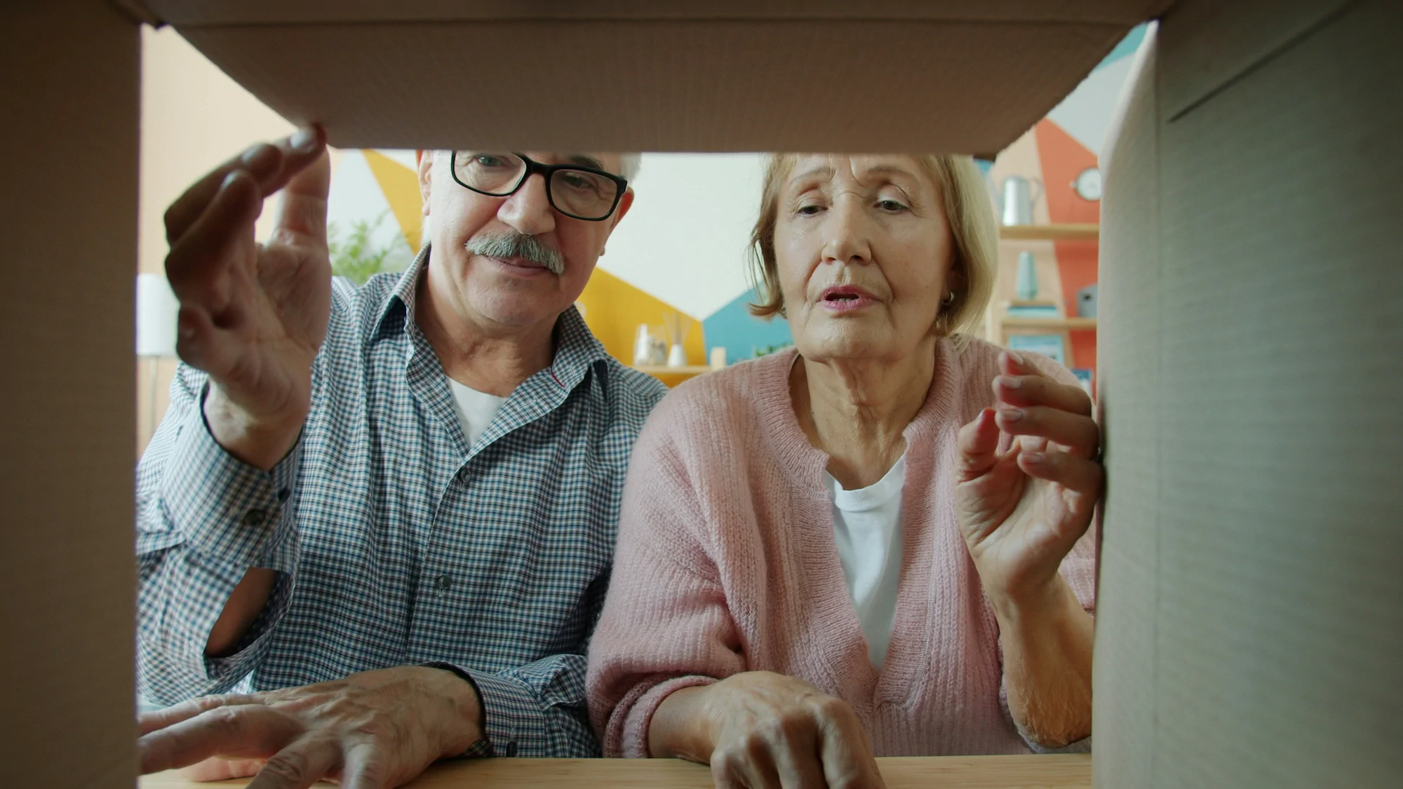 An elderly couple staring into a cardboard moving box.