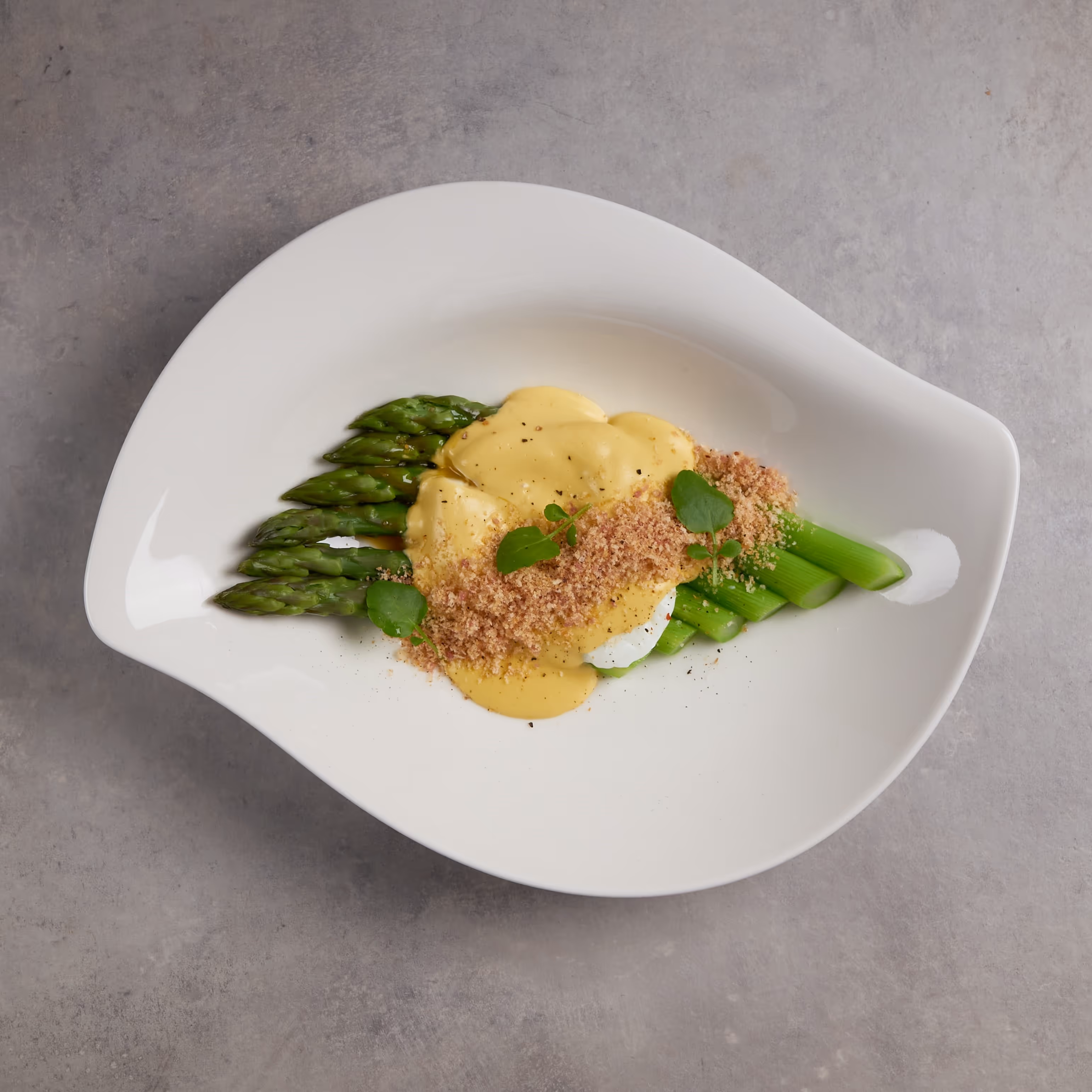 An artfully plated serving of cooked asparagus topped with Hollandaise sauce and a boiled egg