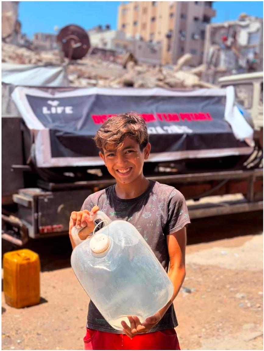 Un enfant tient un bidon d'eau potable devant un camion de distribution de LIFE à Gaza