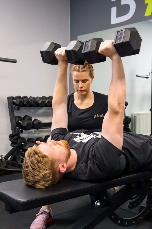 Aidean overseeing a male customer while he completes a benchpress