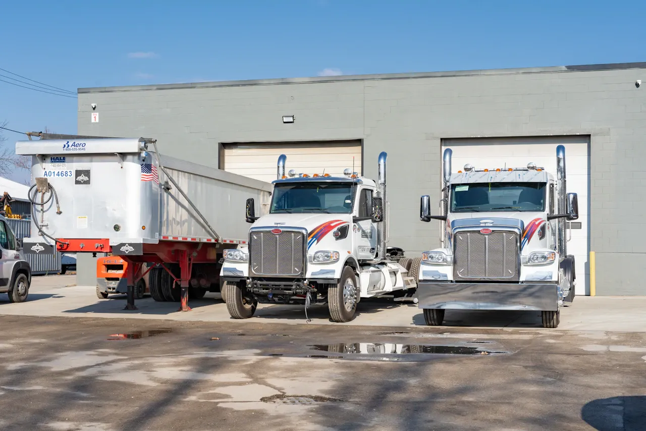 DOT service showing two heavy-duty trucks and dump trailer parked outside commercial repair facility bays.
