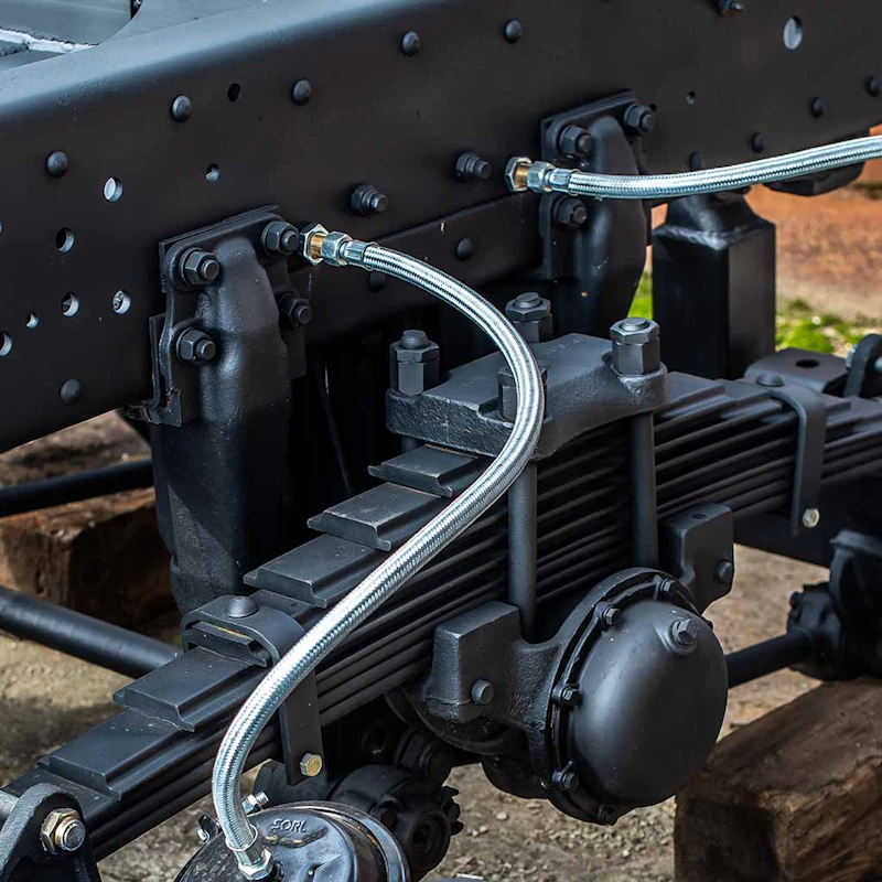Heavy-duty suspension leaf springs and braided brake lines mounted on a truck chassis.