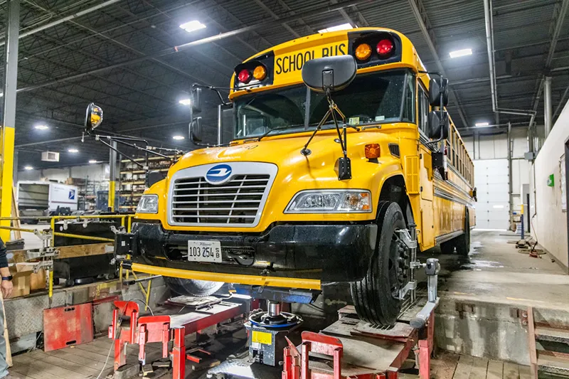 School bus on a wheel alignment rack in a heavy-duty repair shop.