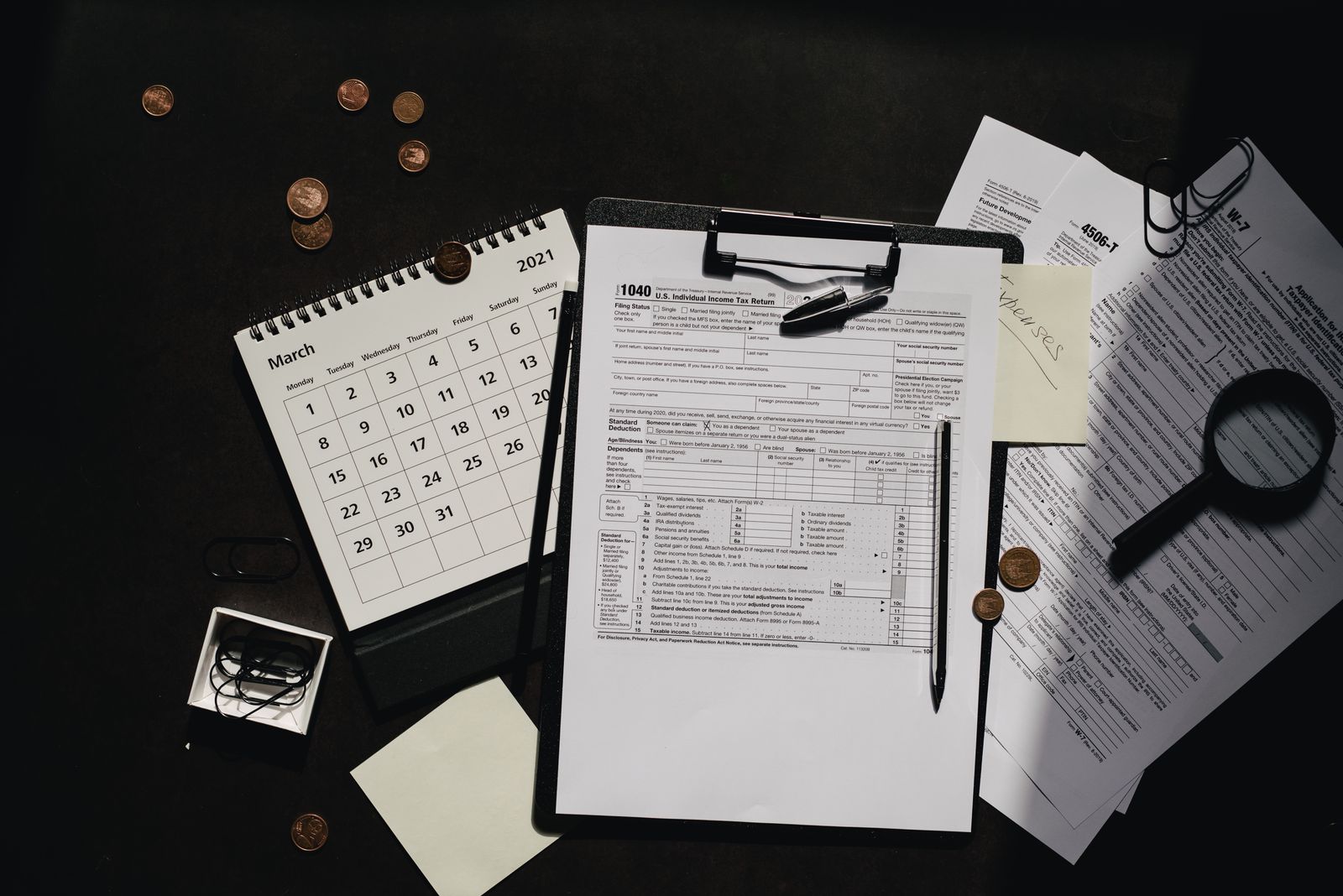 Tax forms on a clipboard with a pen, calendar and magnifying glass