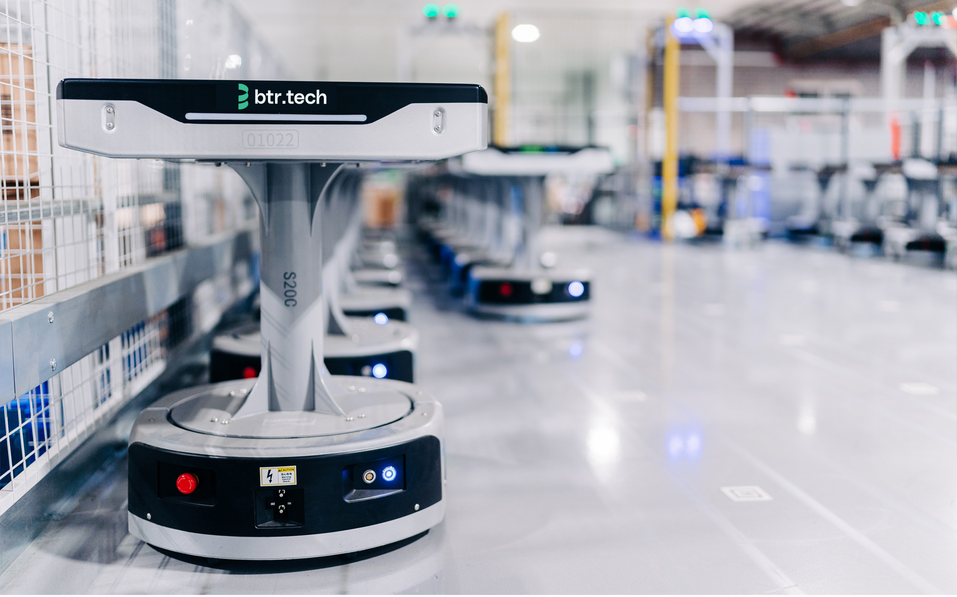 Row of btr.tech branded automated warehouse robots lined up on a factory floor.