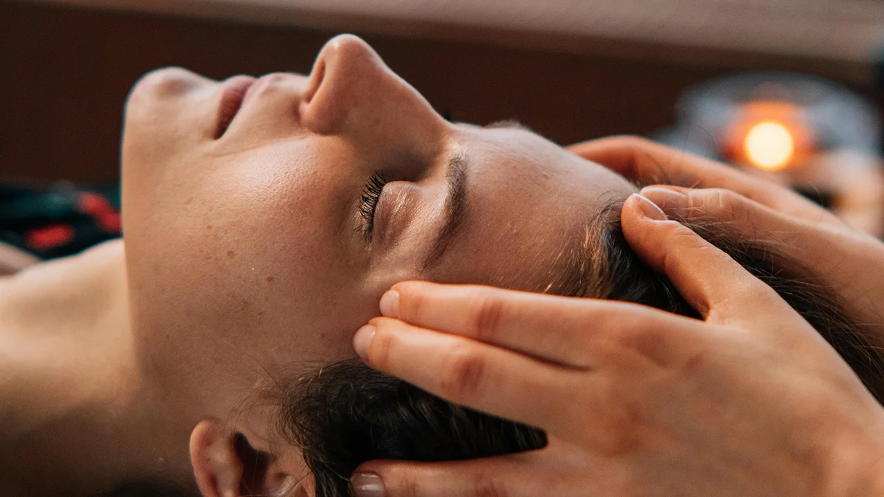 Une personne allongée les yeux fermés reçoit un massage crânien avec des mains pressant doucement ses tempes.