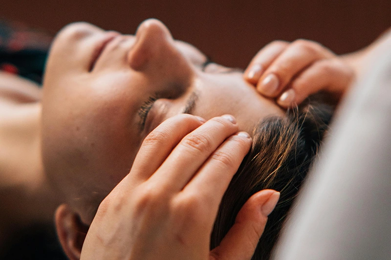 Gros plan sur une personne allongée recevant un massage crânien avec les mains du masseur posées doucement sur le front et les tempes.