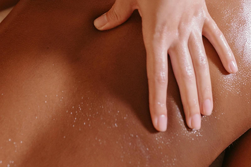 Main posée sur le dos légèrement huilé d'une personne recevant un massage, représentant un massage ayurvédique.