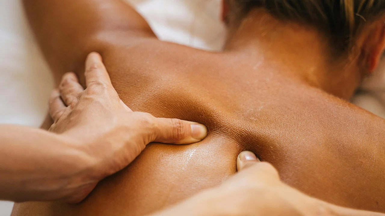 Mains effectuant un massage des tissus profonds sur le dos d'une personne allongée, avec une peau légèrement huilée.