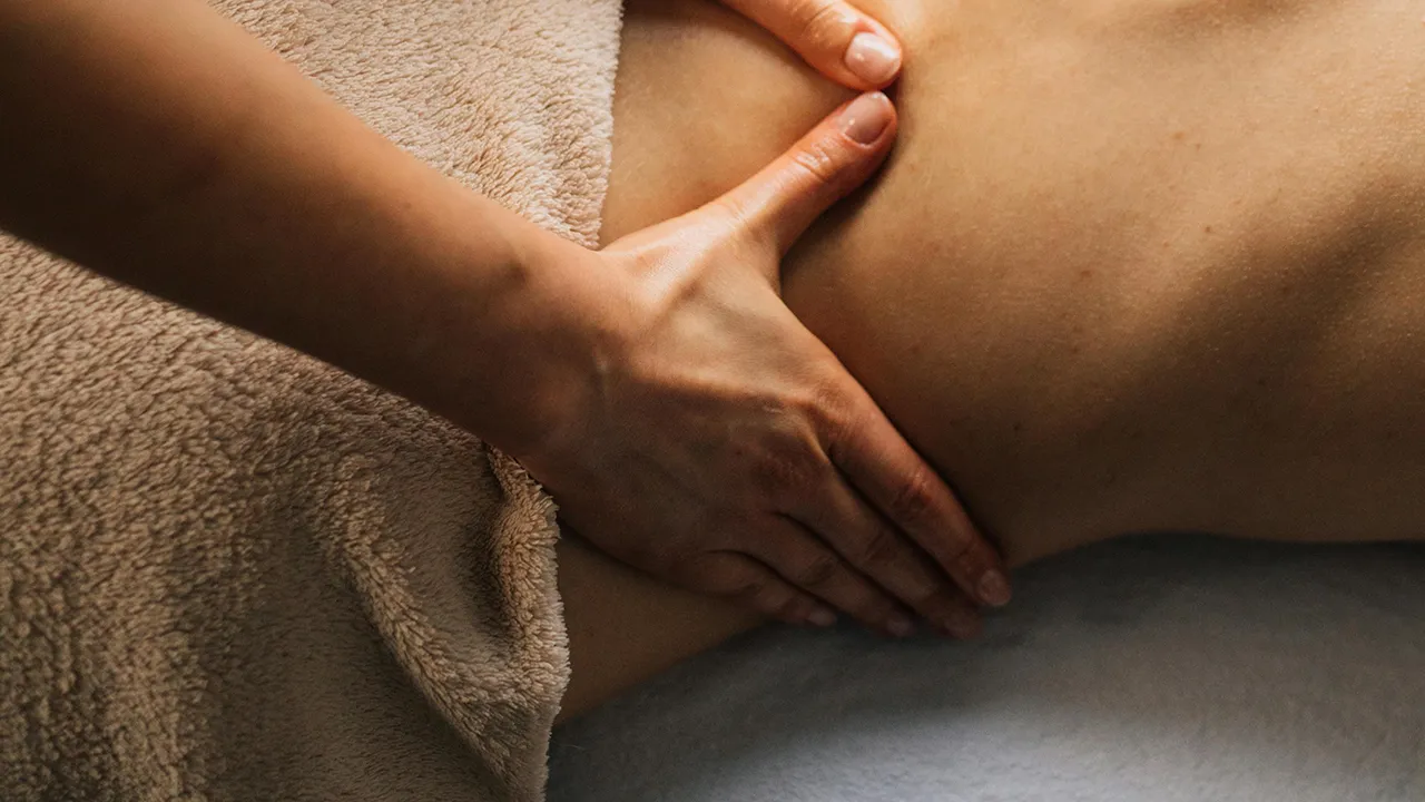 Une main appliquant un massage sur le bas du dos d'une personne allongée sur une serviette beige.
